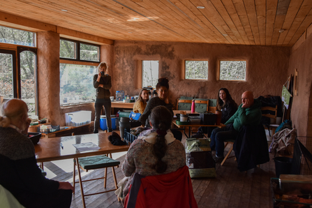 Group of people sitting listening to someone speak in a straw bale building