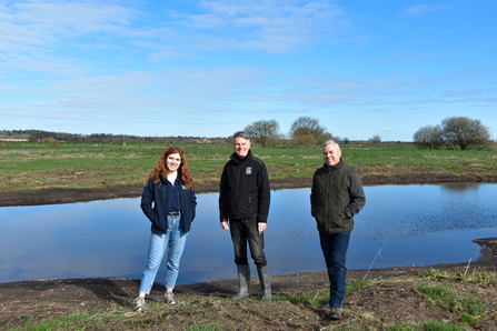 three people stood on farmland in front of pond