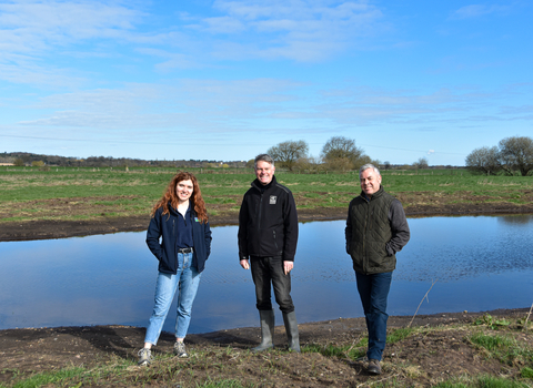 three people stood on farmland in front of pond