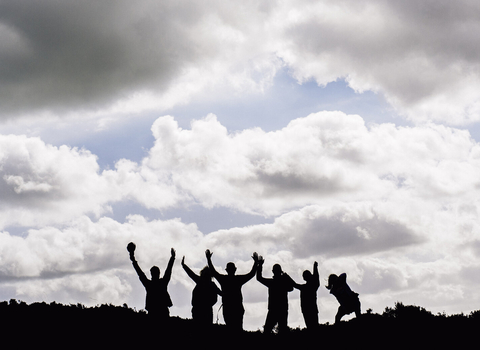 Silhouetted group of people with their arms raised outside on a sunny day