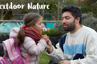 A man helping a young girl blow the seeds from a dandelion