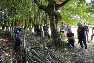 young people smiling whilst building a dead hedge in trees