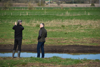 two men talking by a pond on a farm