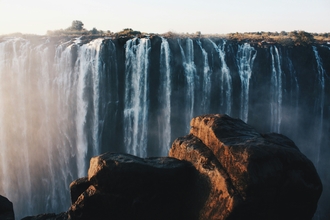 Waterfalls off a large cliff in the distance, rocks in foreground
