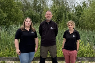 Three people stood infront of a wildlife pond with lots of pond vegetation