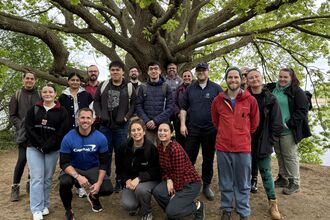 Group of adults stood in front of a large tree under it's boughs