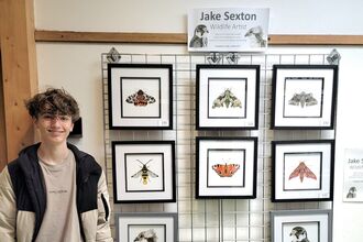 Photo of Jake Sexton next to an exhibition of his art
