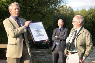 Three men in woodland presenting a picture