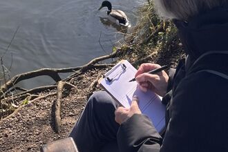 Woman sketching on paper while sitting in front of lake