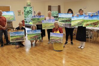 People holding up their paintings at an art workshop