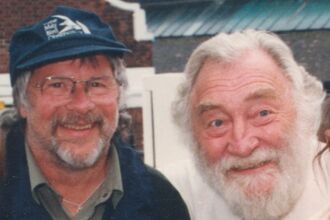 two men with beards and one with glasses and a cap smiling into the camera