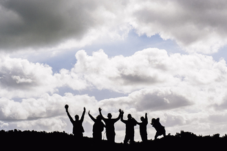 Silhouetted group of people with their arms raised outside on a sunny day