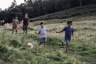 A family smiling as they run down a grassy path in evening sunshine