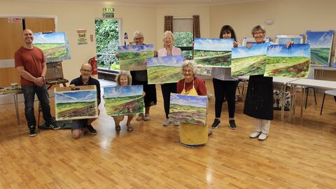 People holding up their paintings at an art workshop