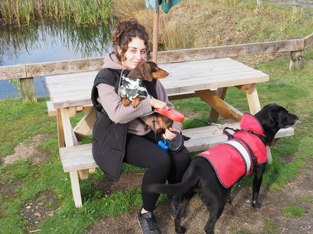 Woman smiling holding a small dog with a big dog on lead