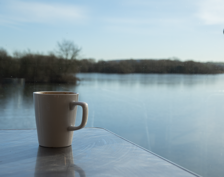coffee cup on a table with view of a pond