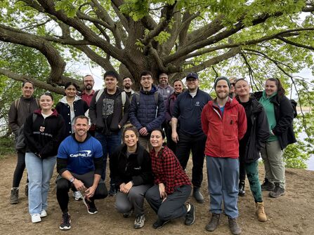 Group of adults stood in front of a large tree under it's boughs
