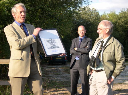 Three men in woodland presenting a picture