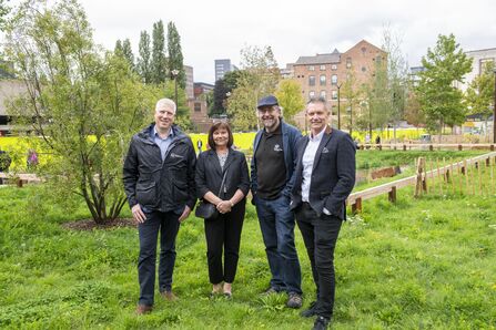 Four people stood on grass infront of a green area of a city centre