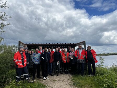  group of people in high vis jackets stood infront of a viewing screen at a nature reserve