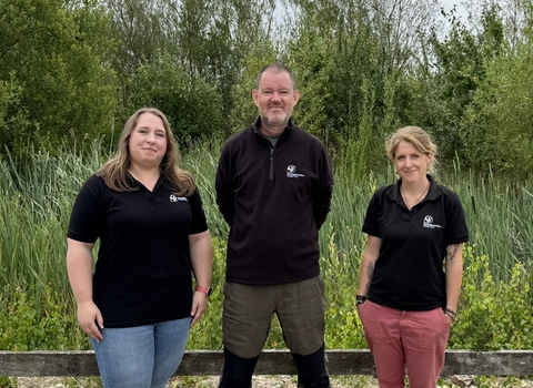 Three people stood infront of a wildlife pond with lots of pond vegetation