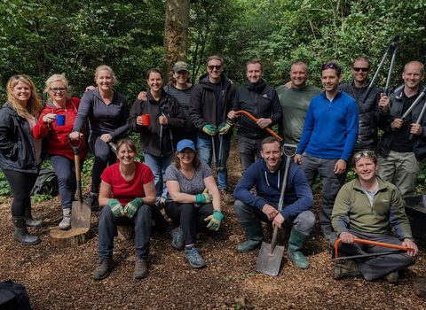 Outdoor volunteers with tools lined up for group photo in front of trees