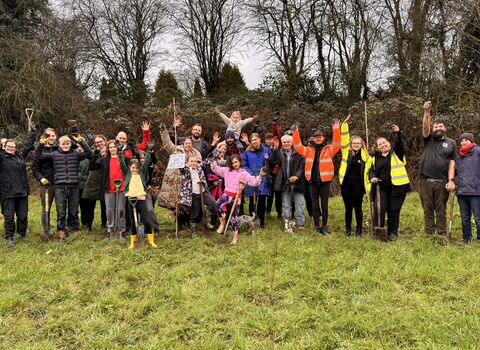 Outdoor volunteers pose for group photo on a grassy field, woodland in background