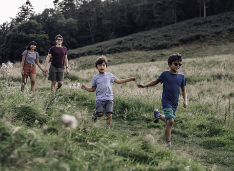 A family smiling as they run down a grassy path in evening sunshine