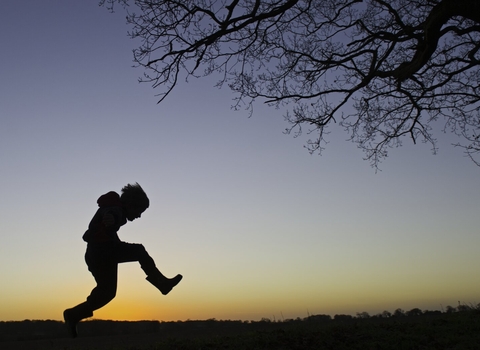 Young boy silhouetted at dusk playing on edge of woodland Norfolk winter 